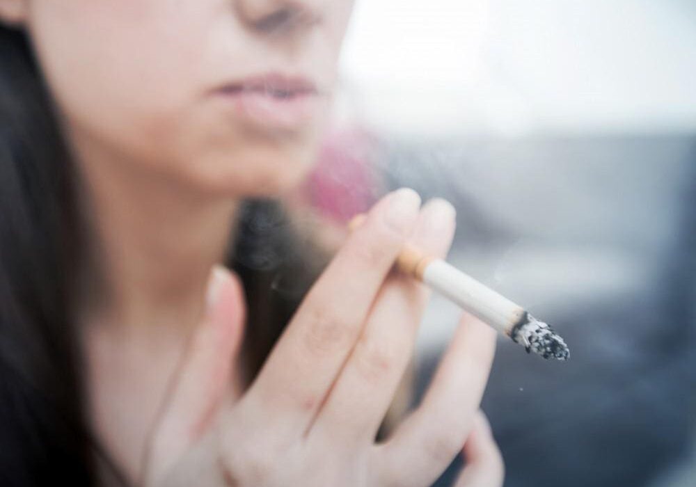 Close-up of a person holding a lit cigarette, about to smoke.