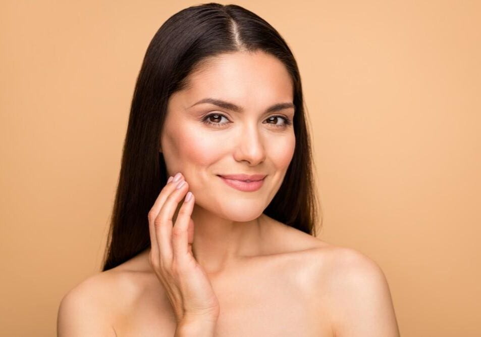 A woman with clear skin gently touching her face, smiling softly.