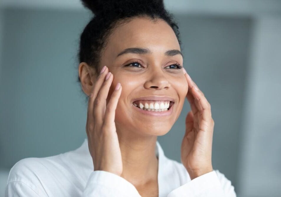 Smiling woman gently touching her face, radiating happiness and calm.
