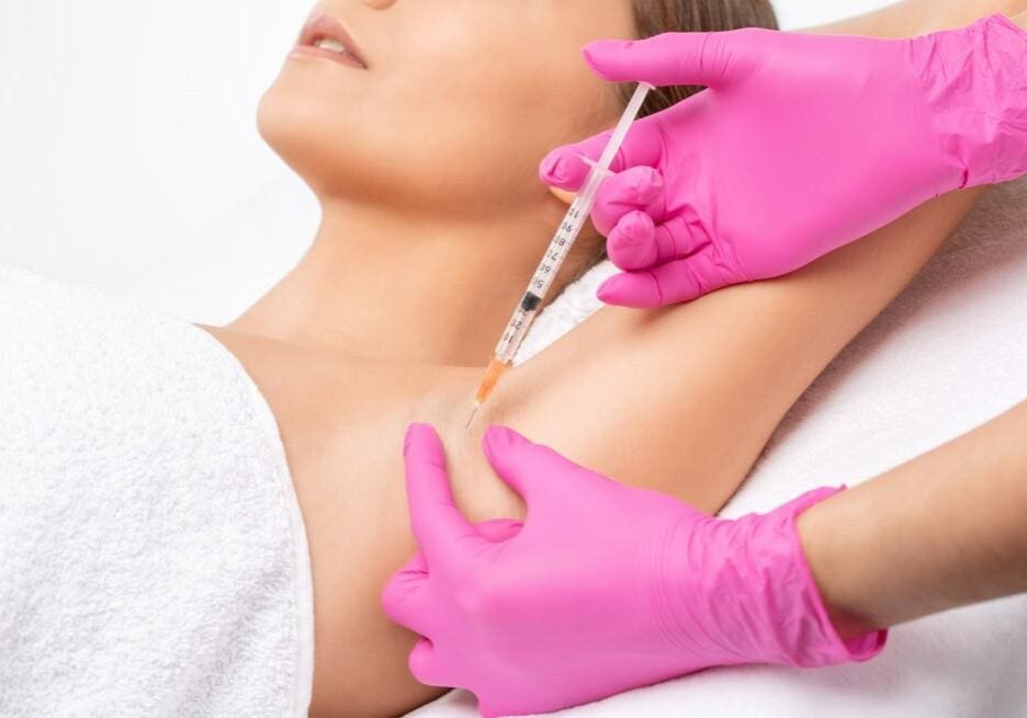 A woman receiving an injection in her underarm from a gloved professional.